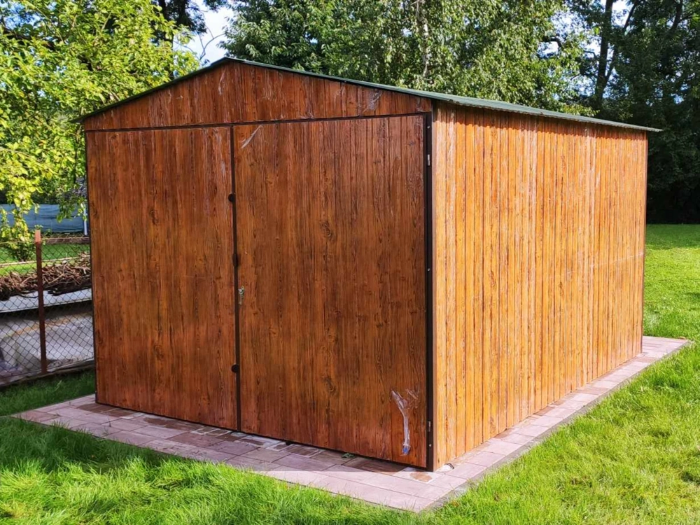 Domek narzędziowy ze stali z drewnopodobnym wykończeniem ustawiony na podłożu z kostki brukowej, otoczony zielonym trawnikiem