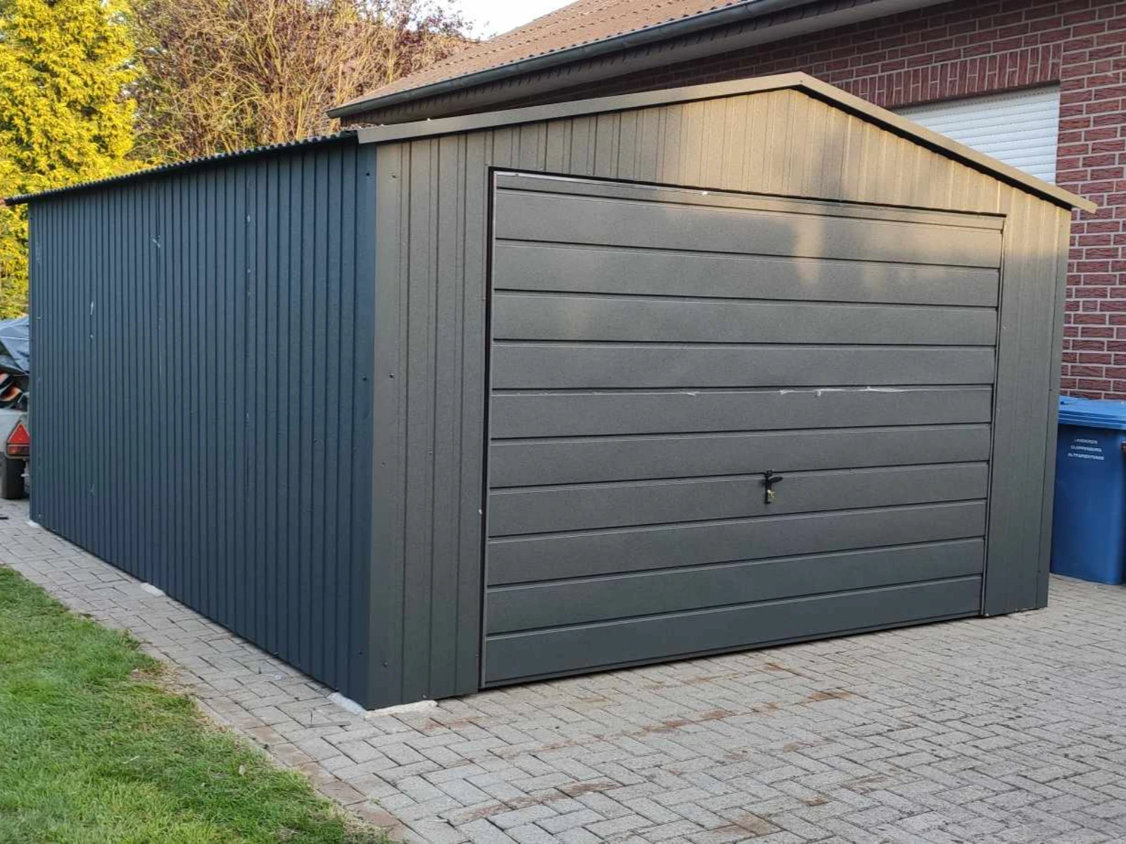 Stalowy garaż blaszany o spadzistym dachu na podjeździe przy domu