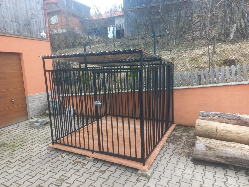 Klatka kennelowa z metalowych prętów z dachem i drewnianą podłogą na utwardzonym podłożu
