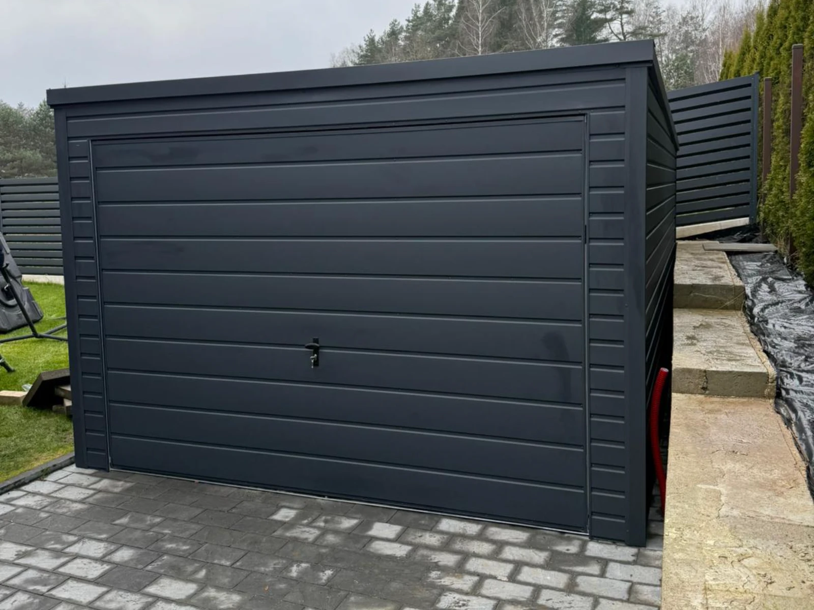 Garaż blaszany z przesuwną bramą w kolorze antracytu na utwardzonej nawierzchni z kostki