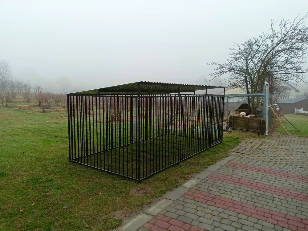 Klatka kennelowa z czarnych metalowych prętów z daszkiem ustawiona na trawniku