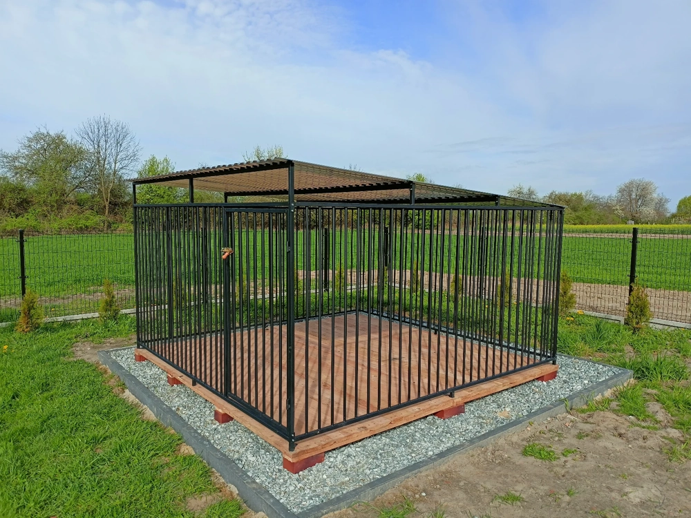 Klatka kennelowa ze stalowymi prętami i zadaszeniem na drewnianej podłodze na trawniku