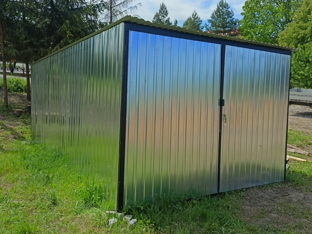 Garaż blaszany ze stalowych paneli na trawniku, z dwuskrzydłowymi drzwiami i czarną ramą przy podłożu
