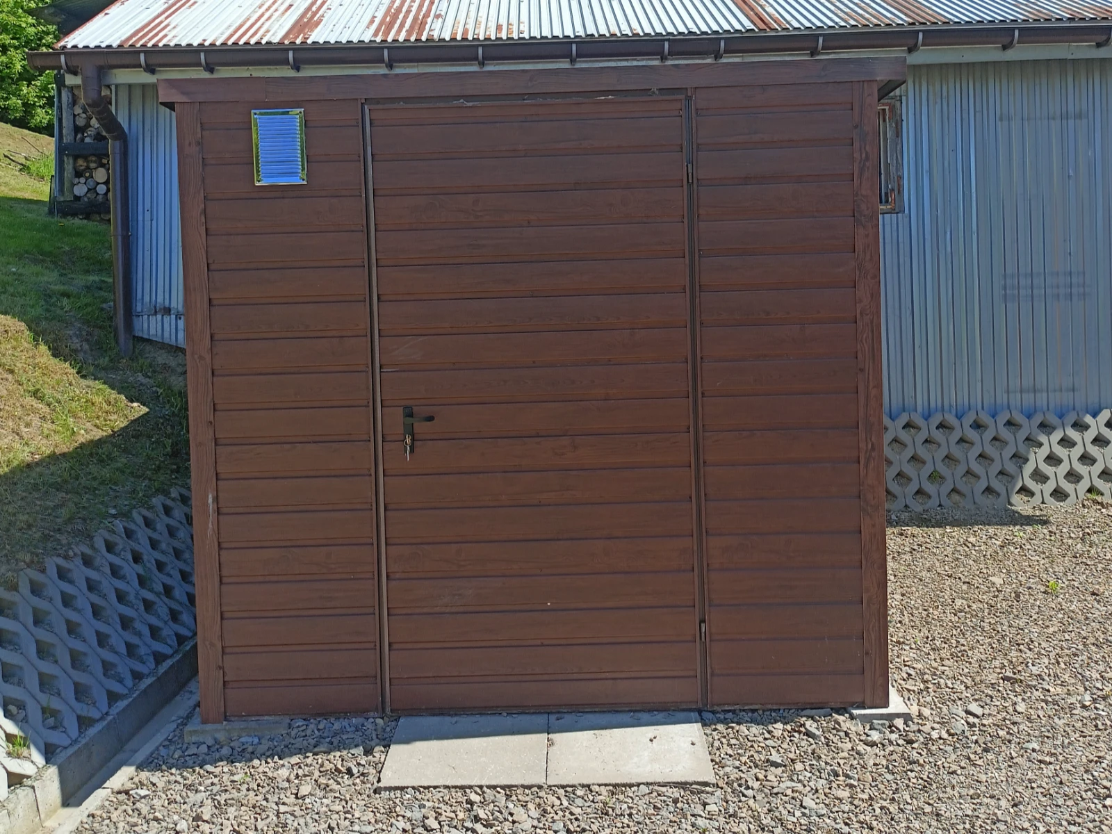 Domek narzędziowy z paneli drewnopodobnych na betonowej płycie z zamykanymi drzwiami