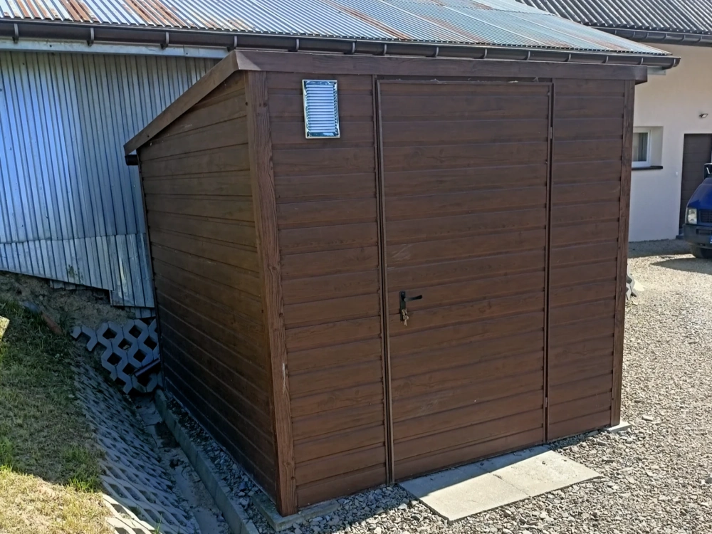 Domek narzędziowy o drewnopodobnej blaszanej konstrukcji postawiony na płytach i żwirze