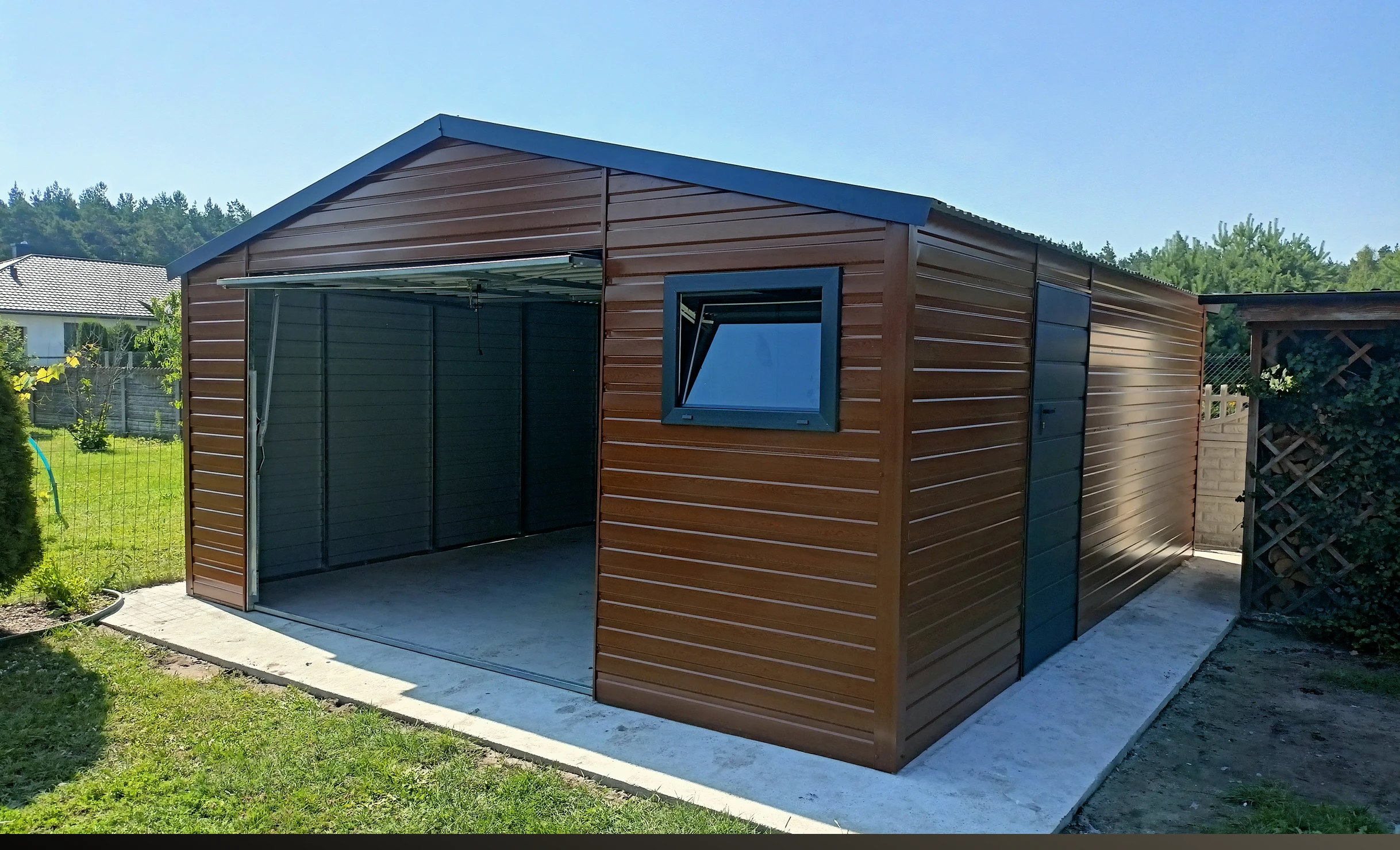 Brązowy metalowy garaż blaszany z drewnopodobnym wykończeniem i otwieranymi drzwiami na betonowej płycie