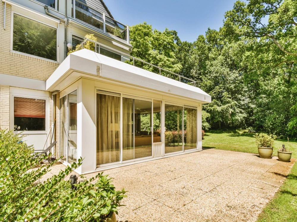 Ogrody zimowe ze stalową konstrukcją, przeszkloną ścianą i tarasem na tle bujnej zieleni