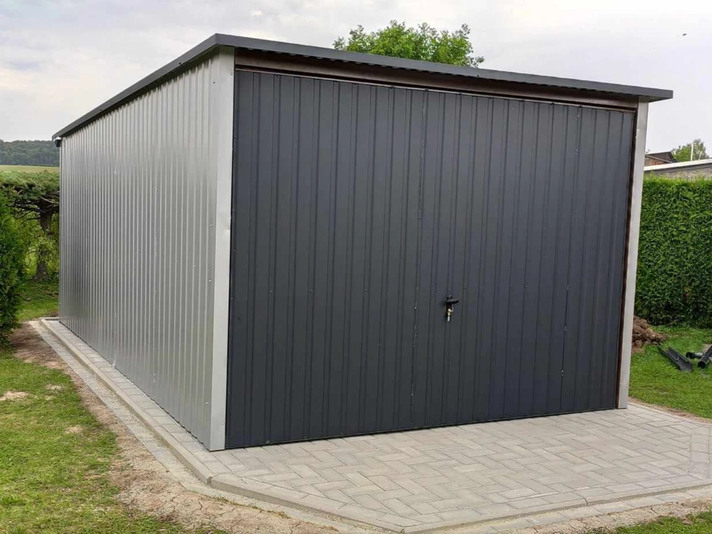 Grafitowy garaż blaszany na podmurówce z kostki brukowej w ogrodzie