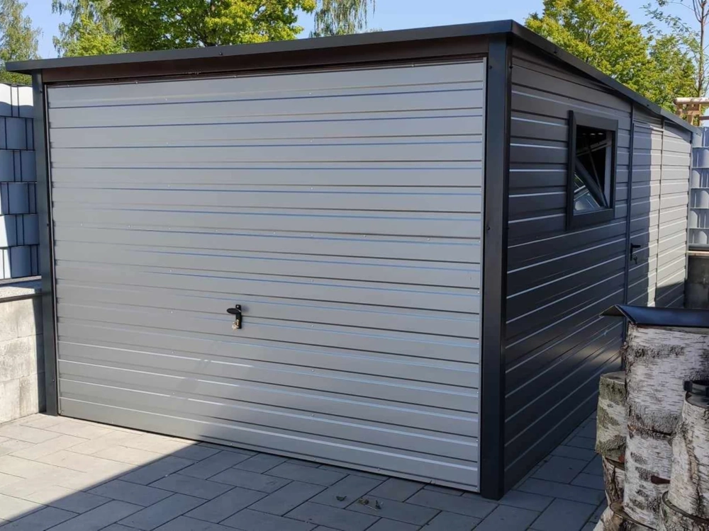 Szary garaż blaszany z bocznym wejściem i oknem na podjeździe z kostki brukowej
